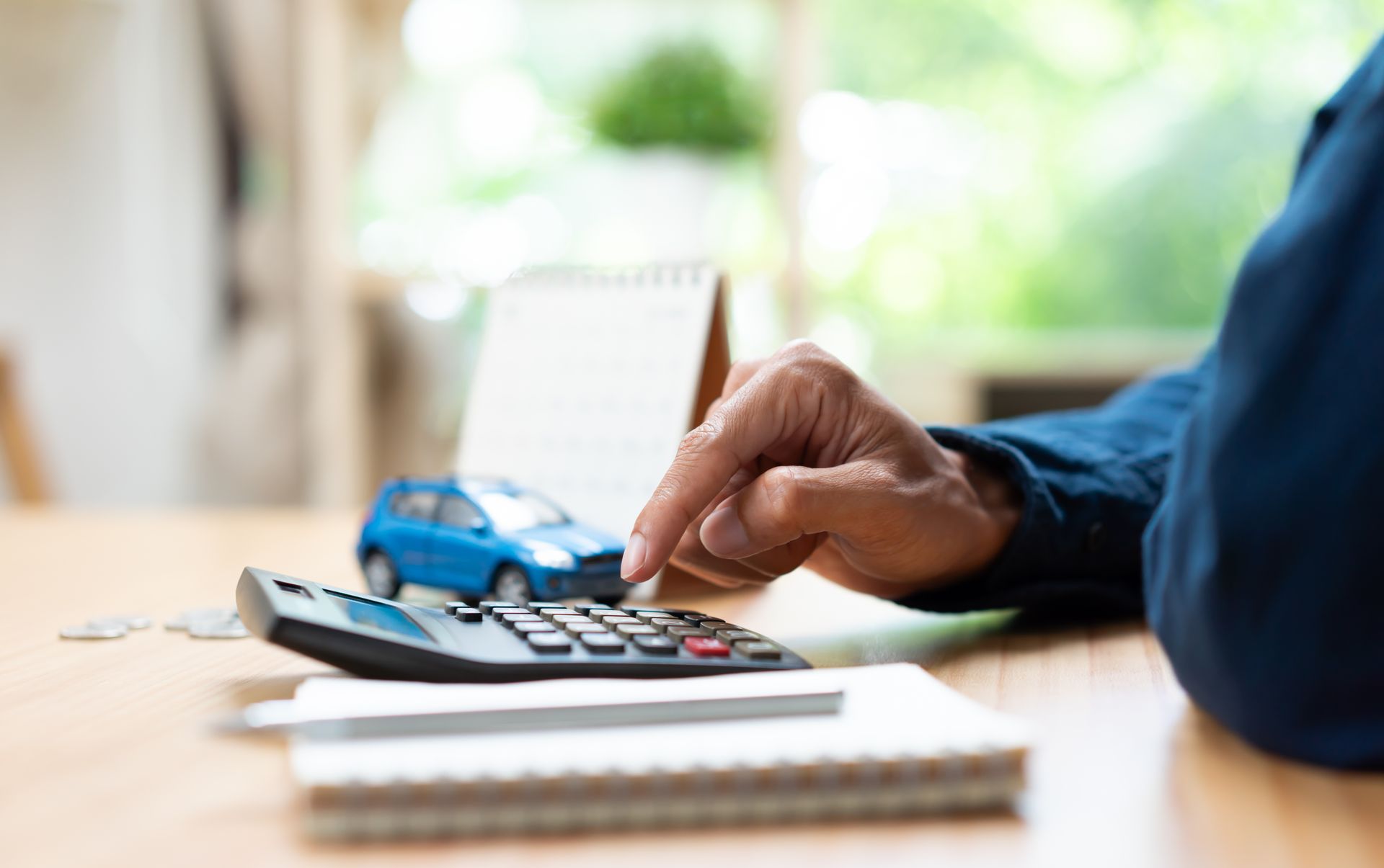 Person using a calculator beside a toy car and notepad to estimate vehicle-related expenses.
