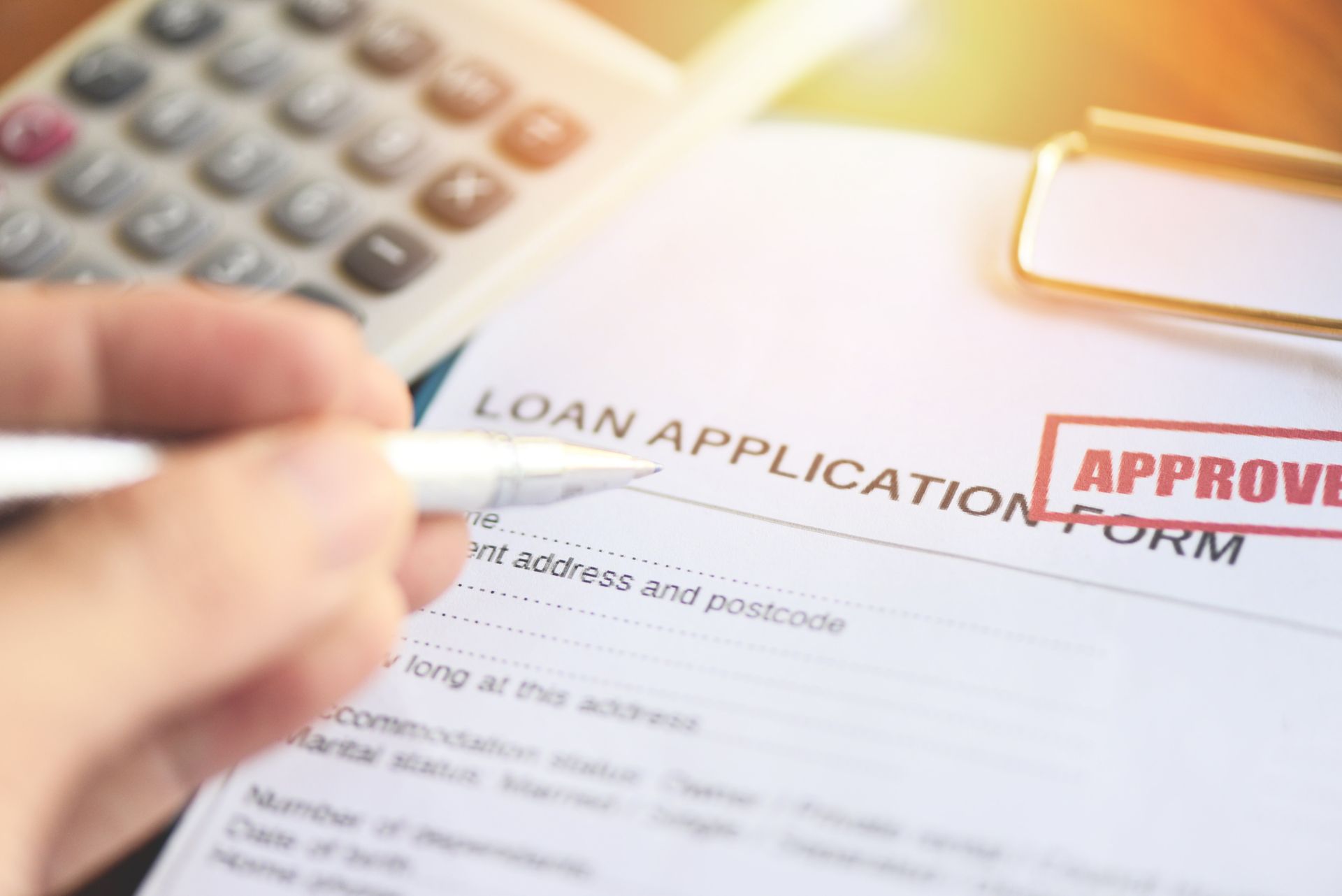 Loan application form marked approved with a pen and calculator on the desk.