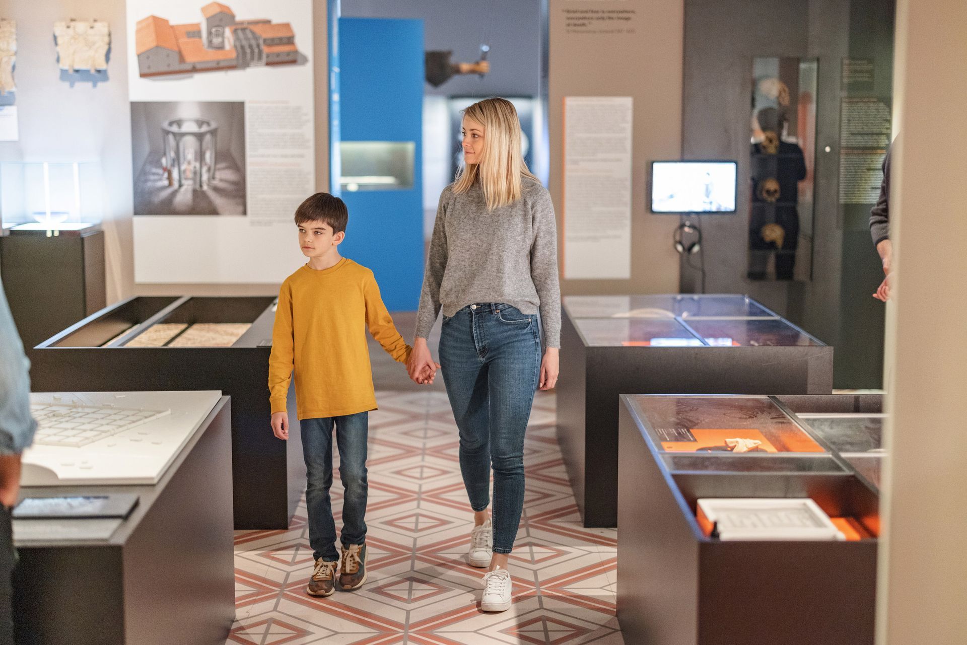 A woman and a boy are walking through a museum holding hands.