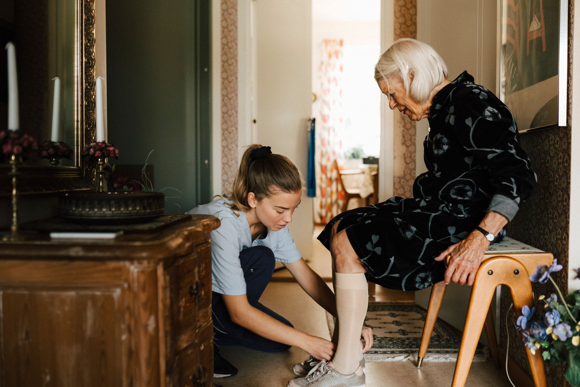 A caregiver helps a senior woman put on shoes, showcasing personal care assisted living.