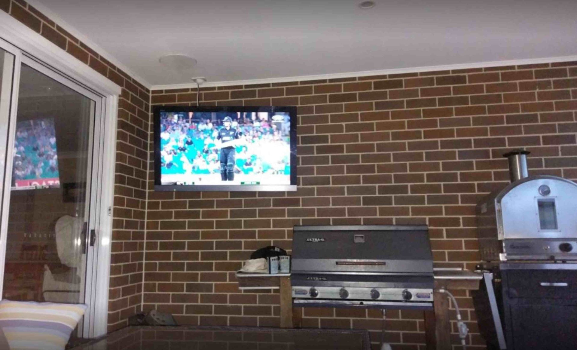 A television is hanging from the ceiling in a room with a brick wall.