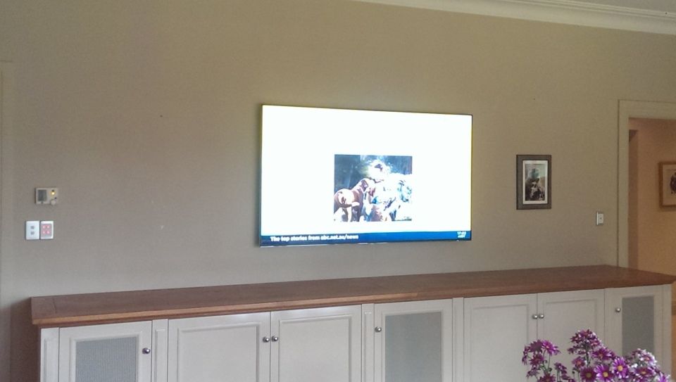 A flat screen TV is mounted on a wall above a wooden cabinet.