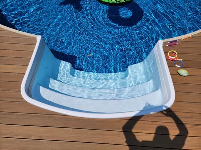 A shadow of a person is cast on a wooden deck next to a swimming pool