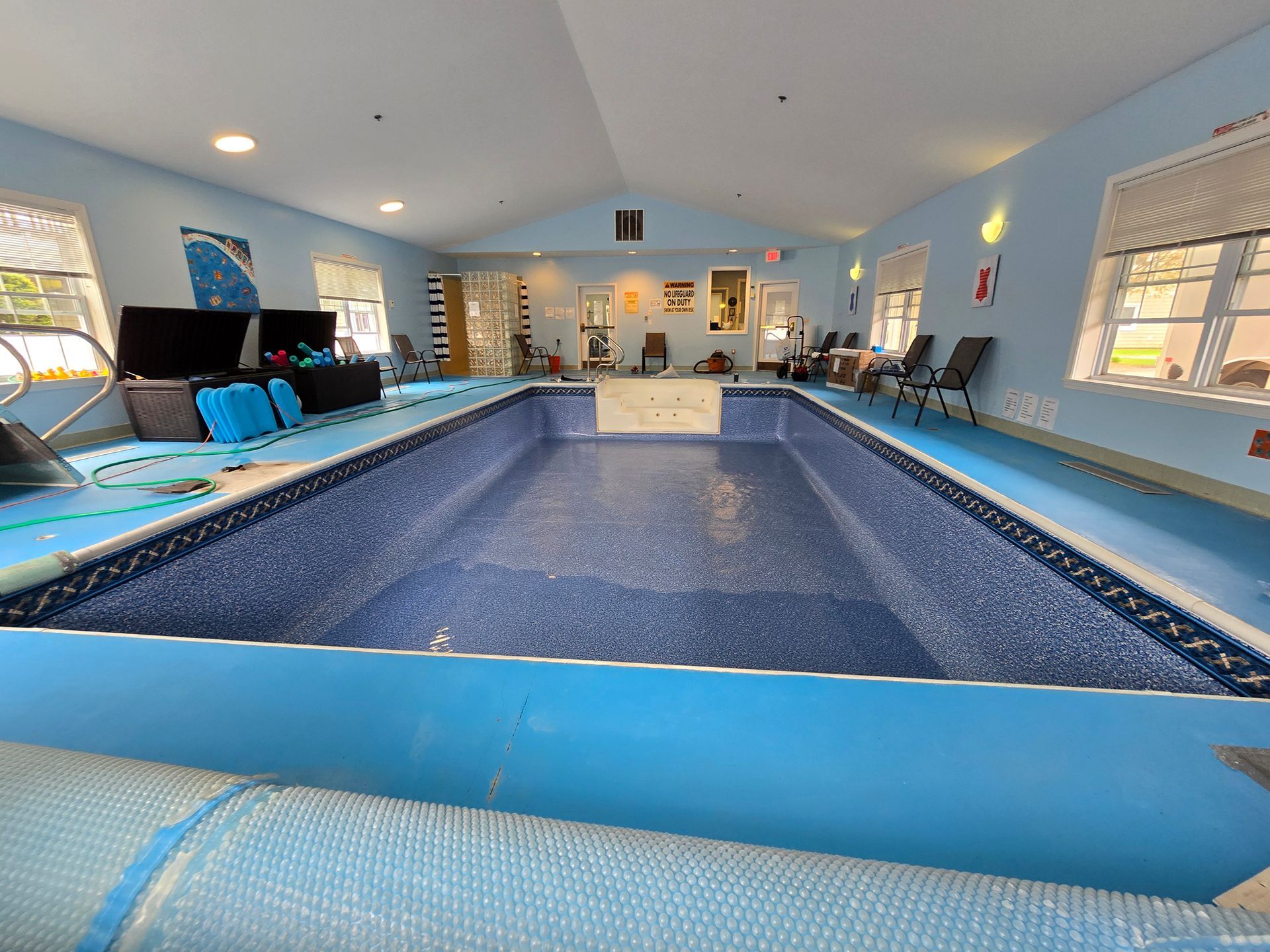 A large indoor swimming pool is surrounded by chairs and windows.