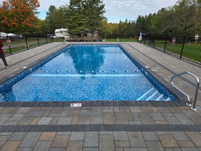 A large swimming pool is surrounded by a brick patio and trees.