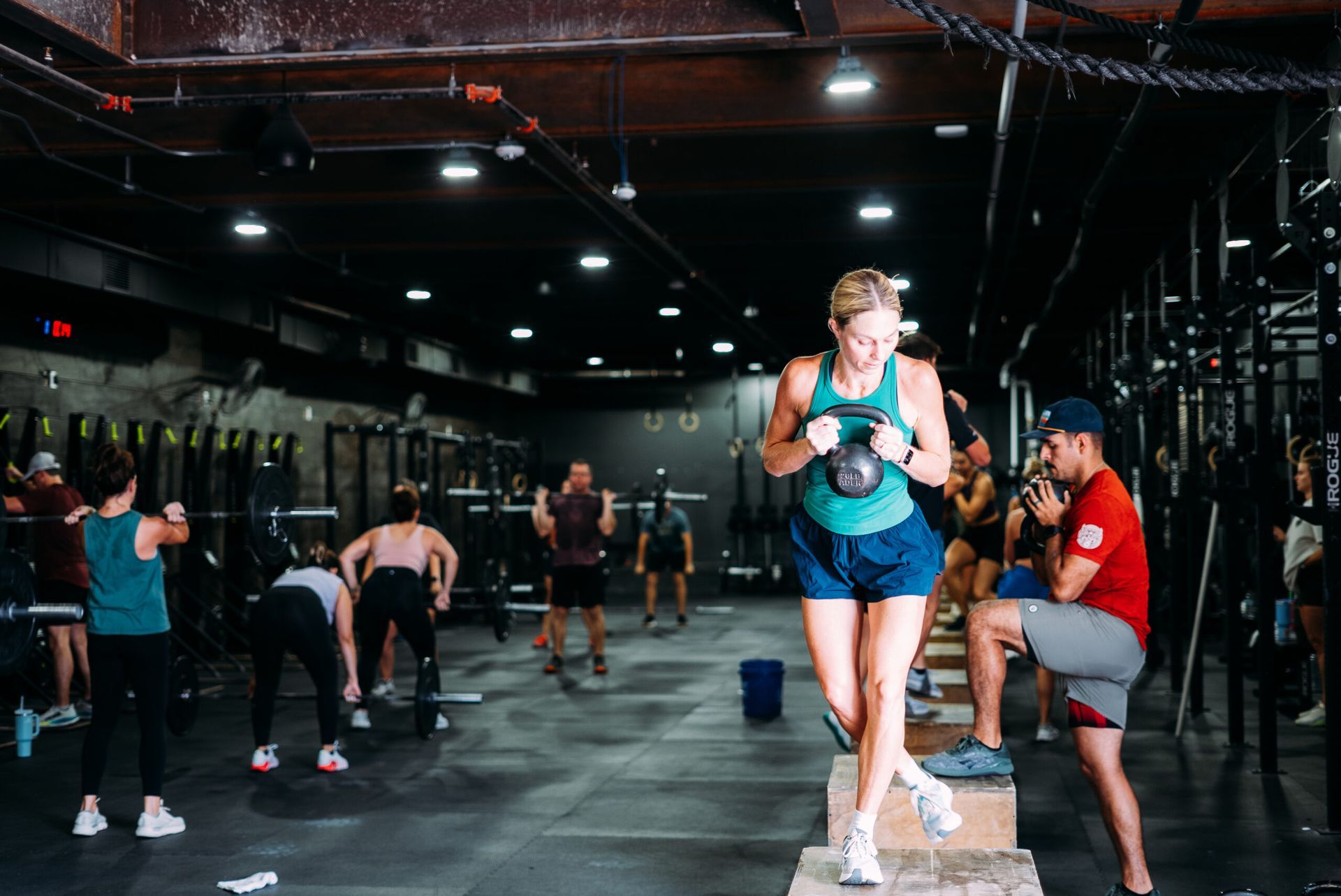 CrossFit gym with athletes warming up, one runner in a blue tank and cap in front