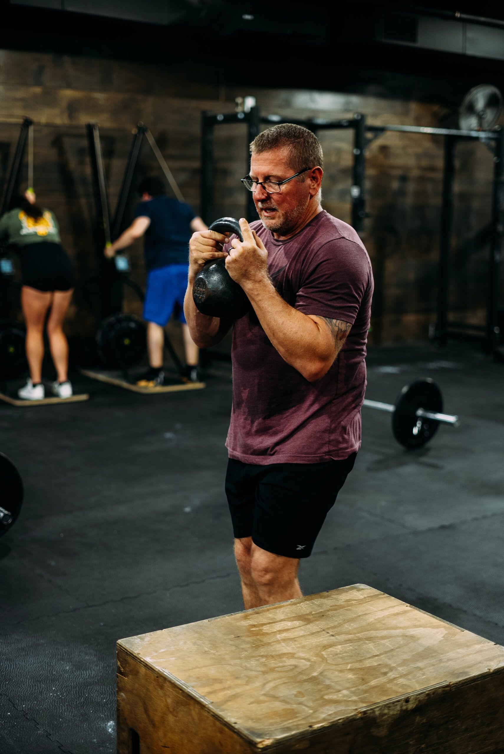 Man in maroon shirt boxing beside a wooden plyo box in a gym