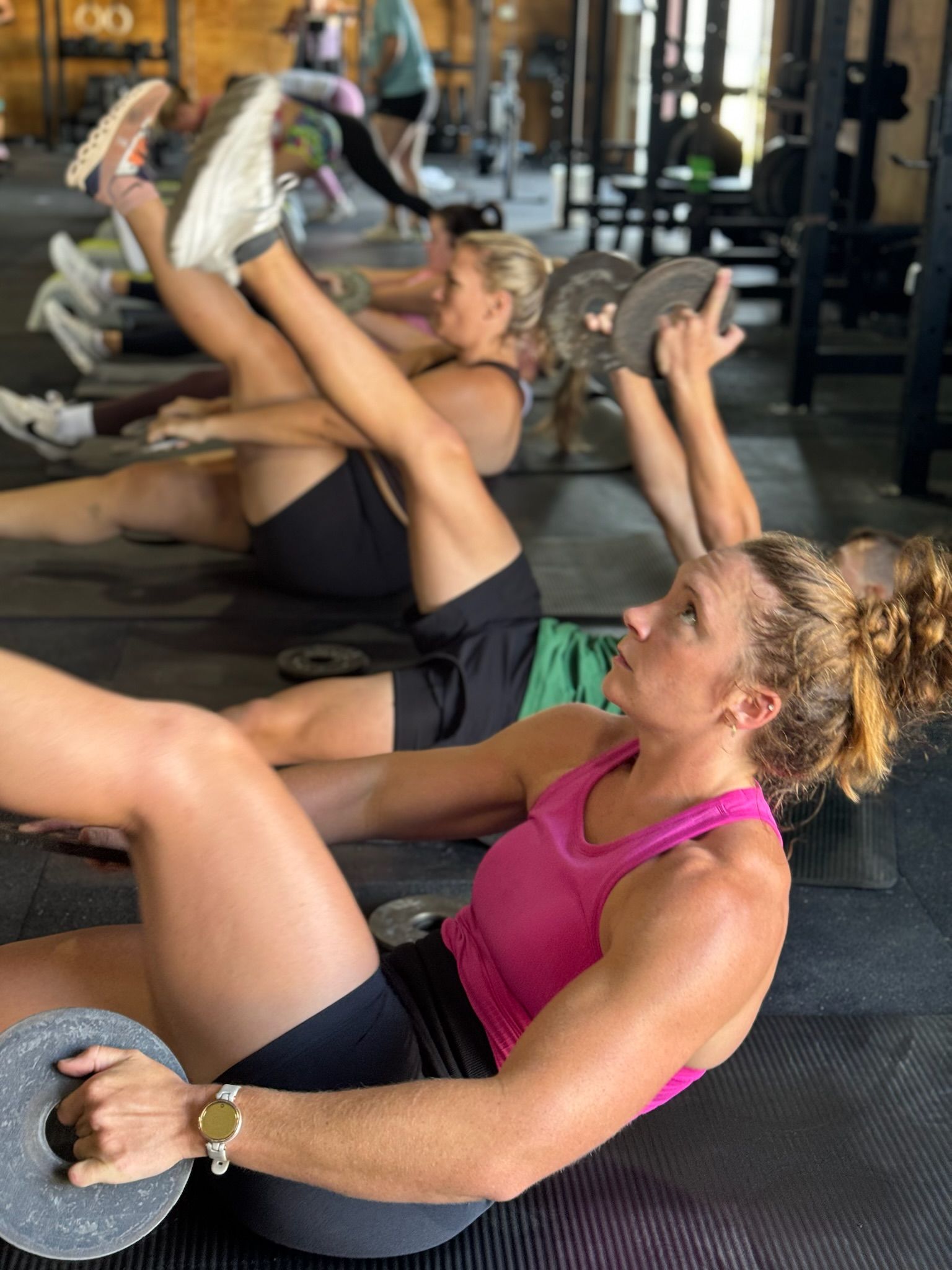 People doing core exercises on mats in a gym, with one woman in a pink top in the foreground