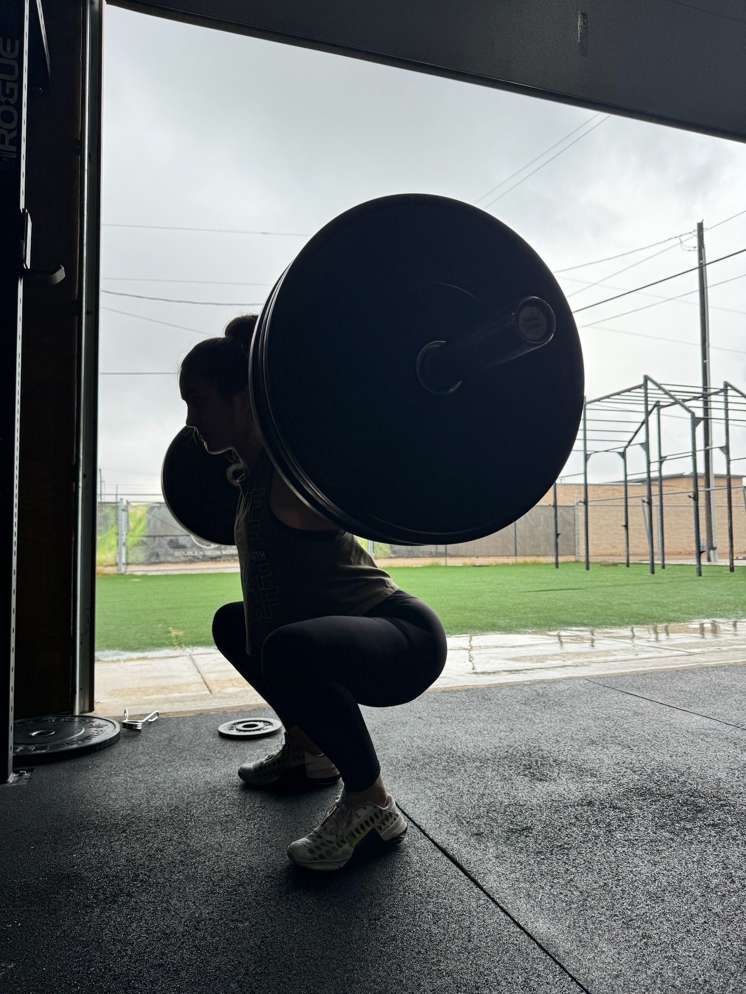 Person in a squat with a barbell in a gym opening, backlit by daylight