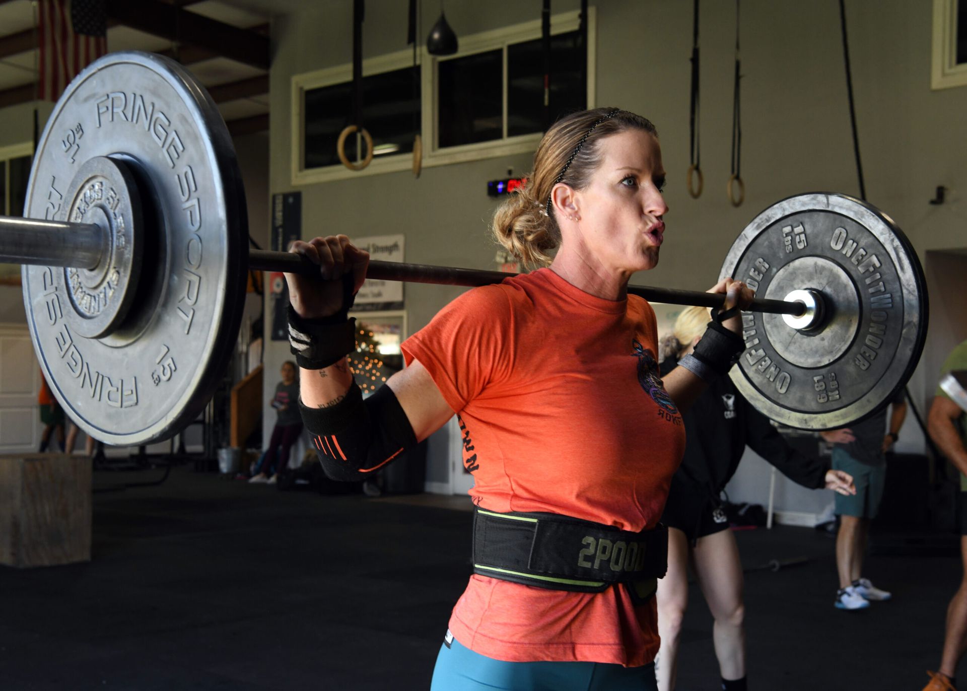 Woman in orange shirt lifting a barbell during a gym workout
