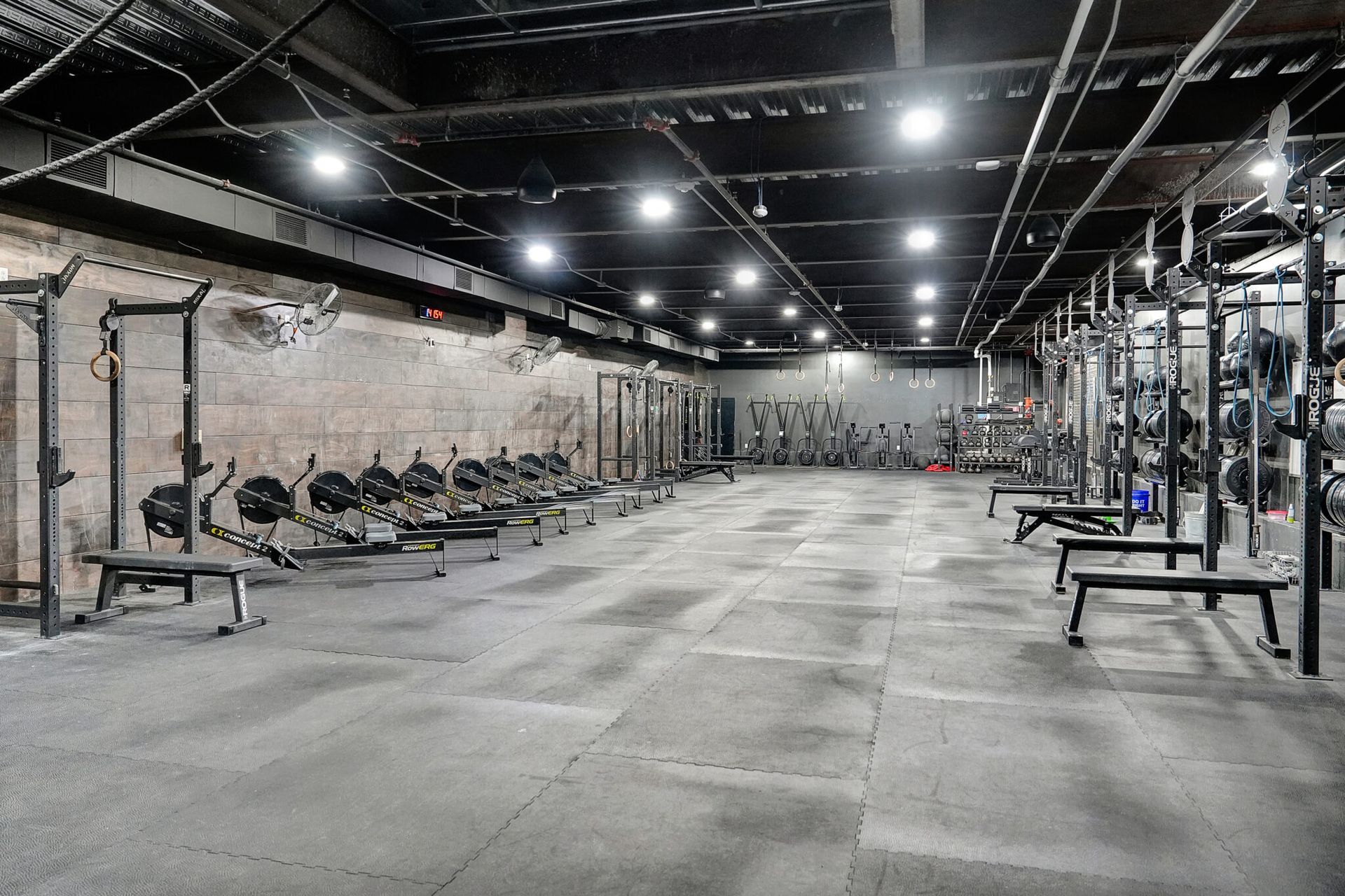 Empty gym with weights, rowing machines, and racks under bright industrial lighting