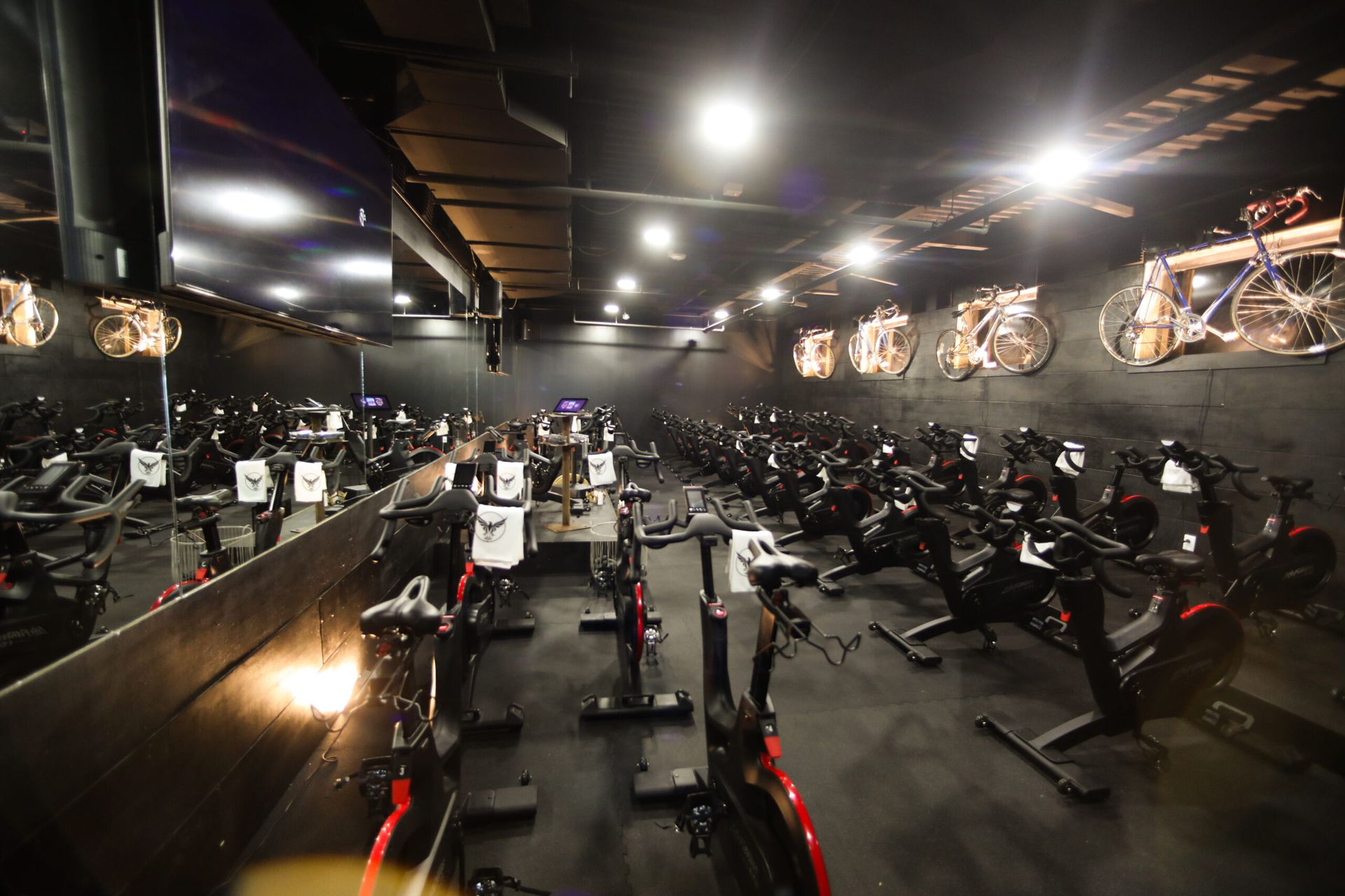 Indoor gym with rows of exercise bikes and bright ceiling lights, seen from the front.