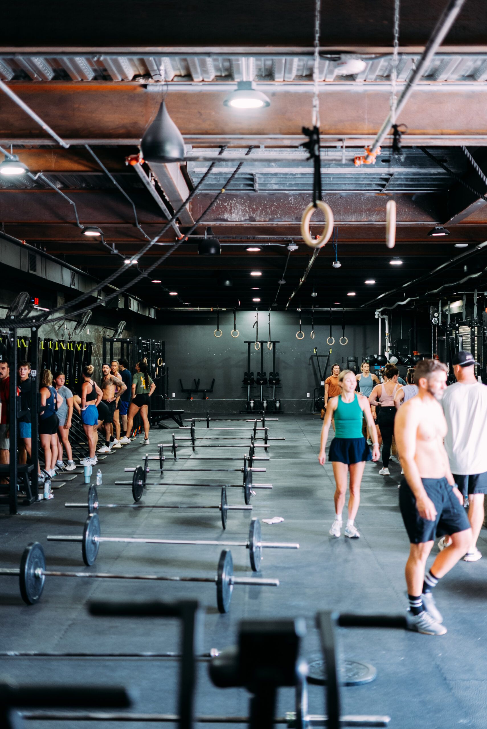 Group exercising in a CrossFit gym with barbells, rings, and people walking between workout stations