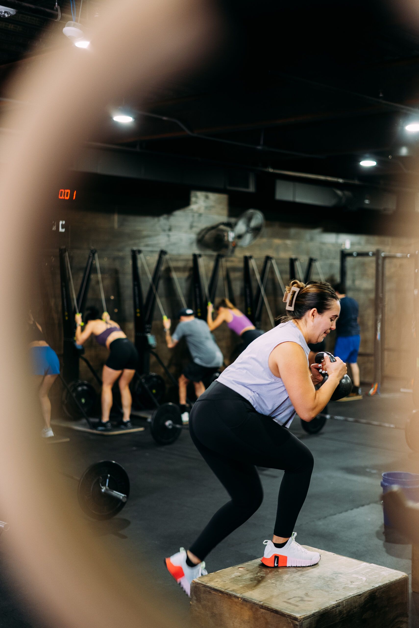 Woman doing a squat on a box in a gym class, with others exercising in the background.