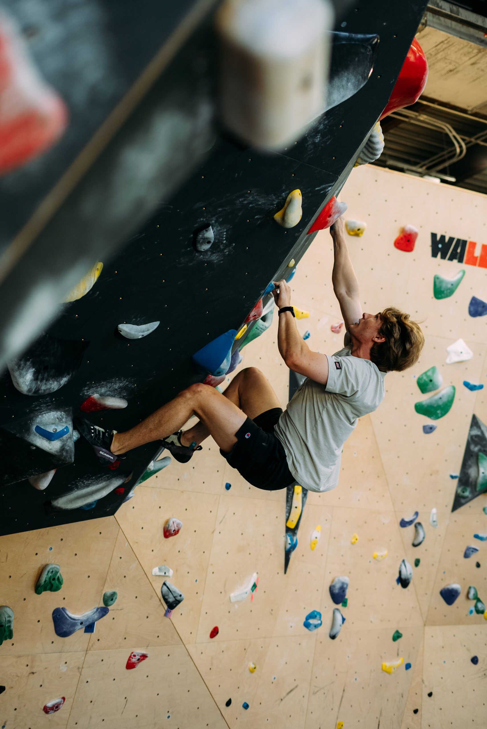 Person rock climbing indoors on a steep wall with colorful holds and safety rope