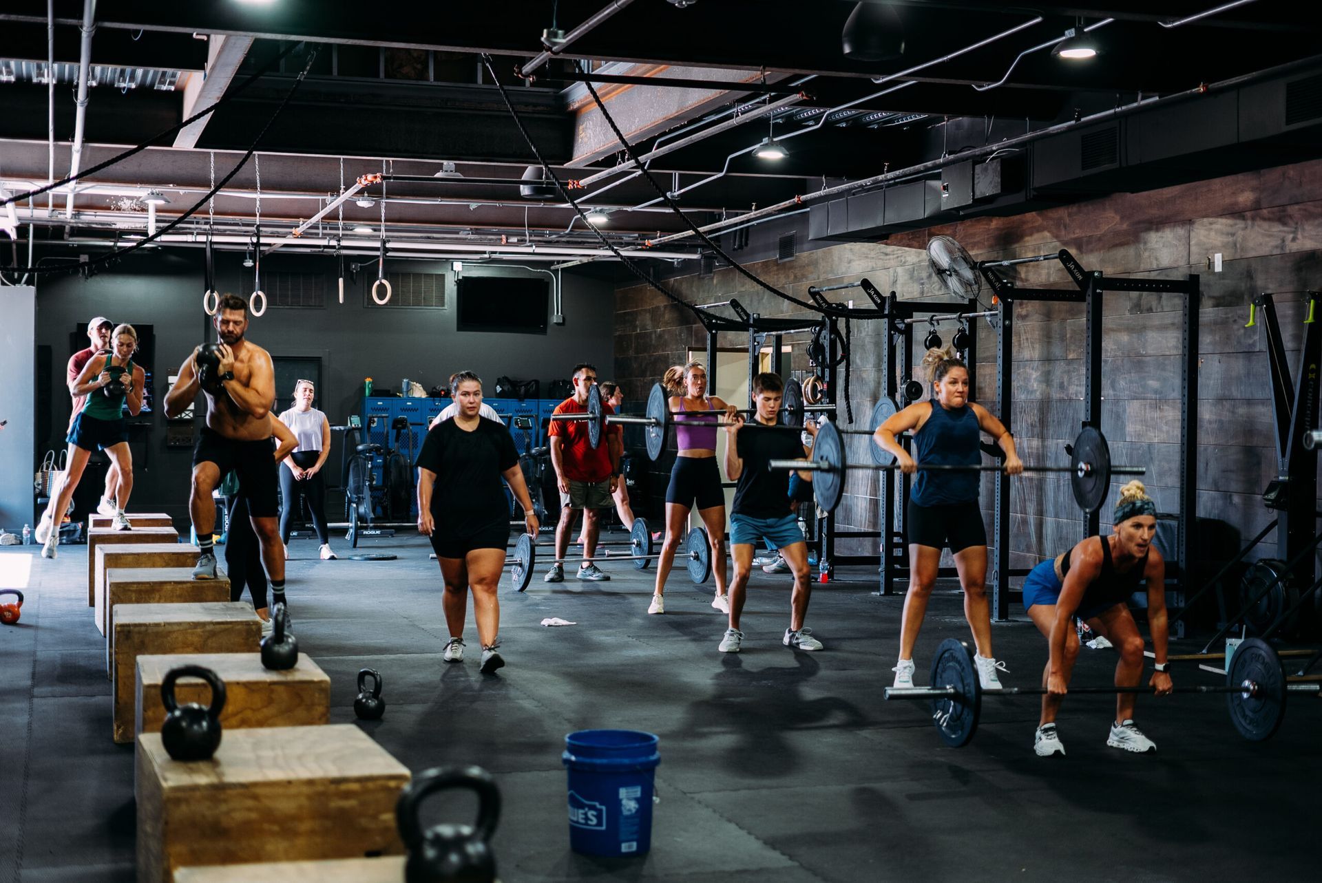 People exercising in a gym class with dumbbells and kettlebells on the floor