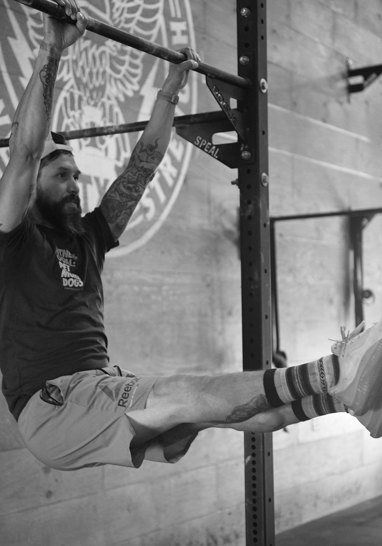 Man doing hanging leg raises on a pull-up rig in a gym, with one leg extended and one bent.