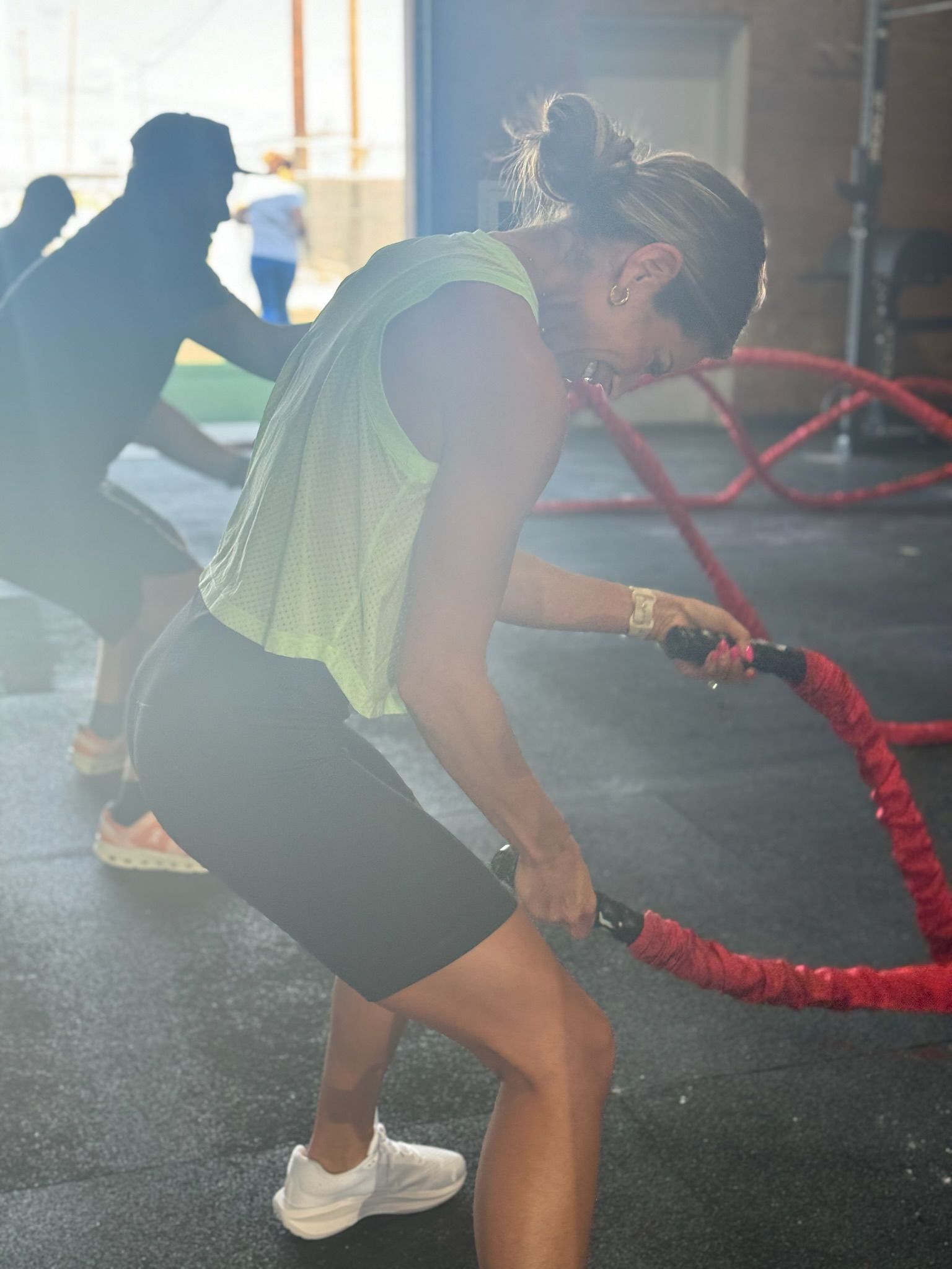 People doing battle rope exercises in a gym, with one person in a neon top in the foreground.
