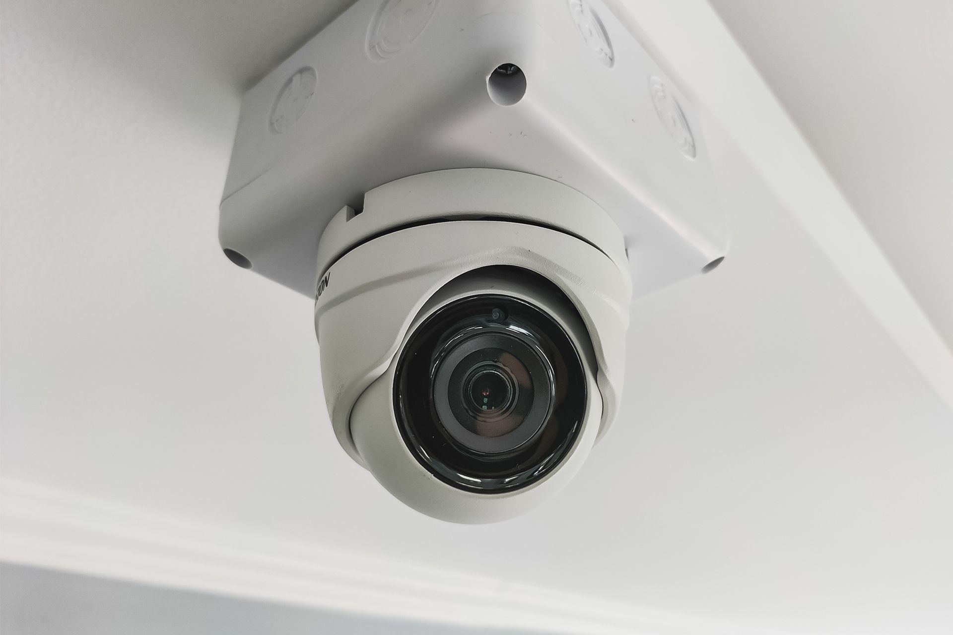 White security camera mounted on a white ceiling, angled down.