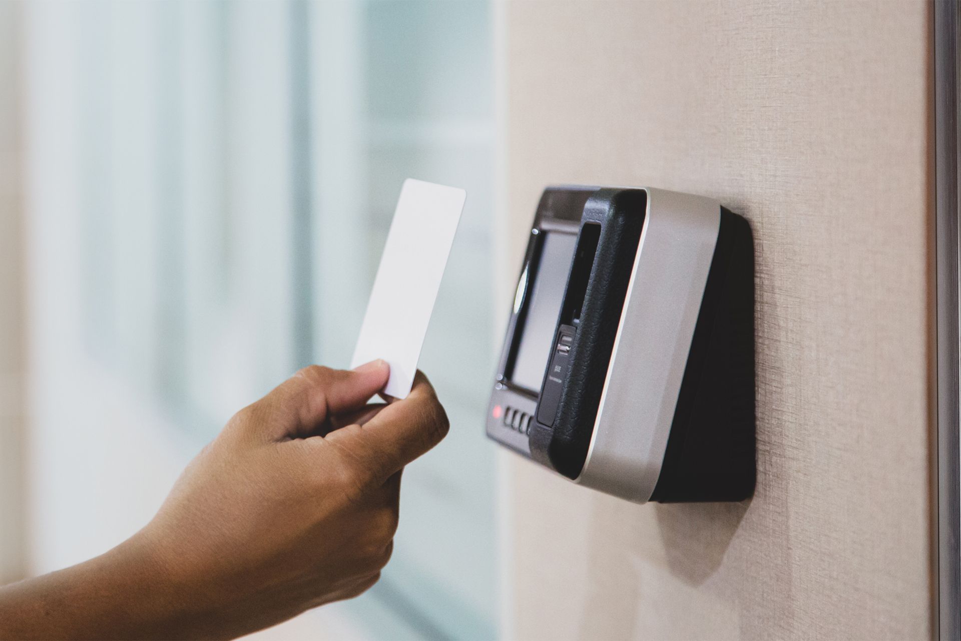 Hand holding access card near a security reader on a wall.