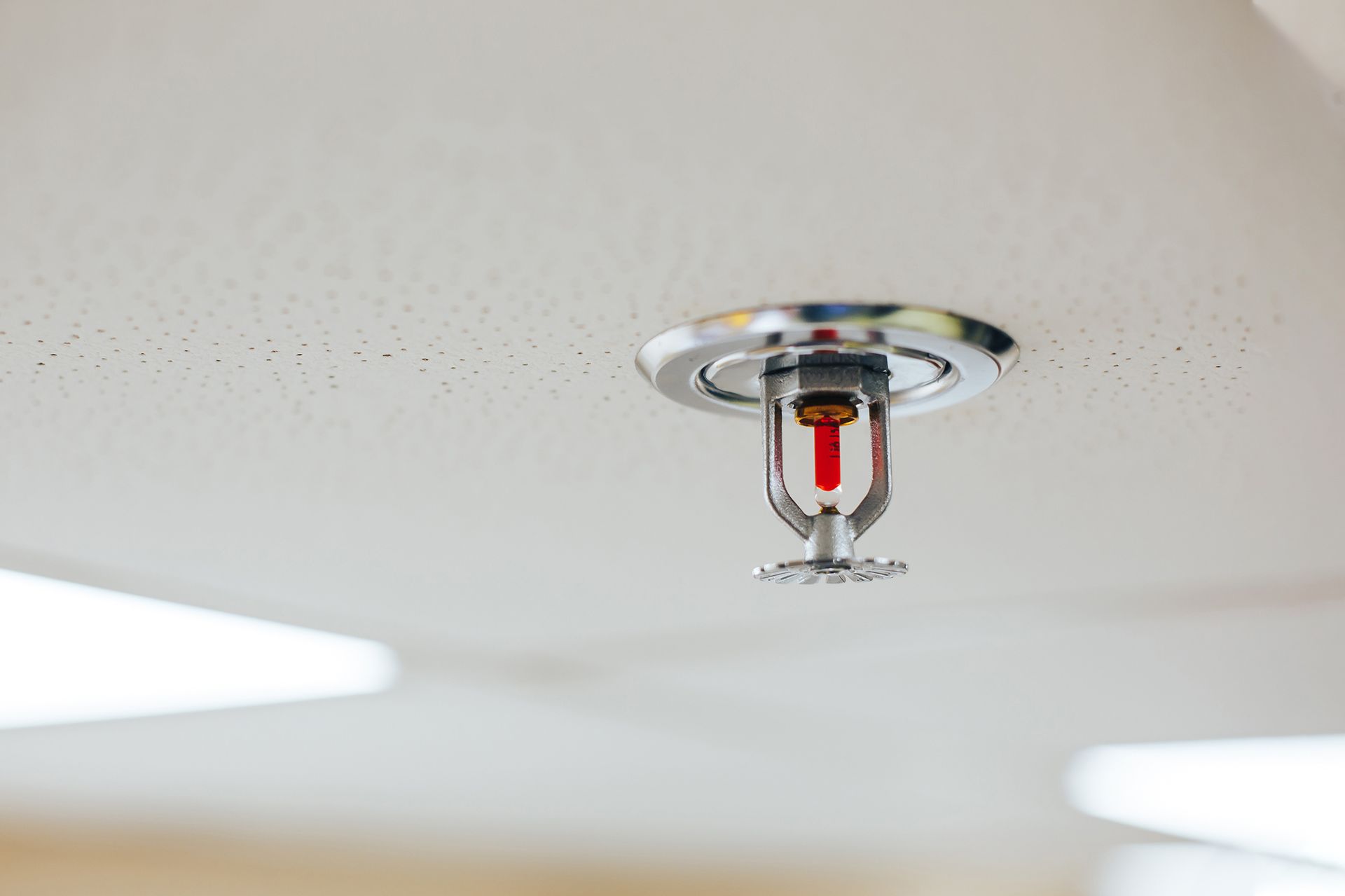 Hand testing a white smoke detector mounted on a white ceiling.