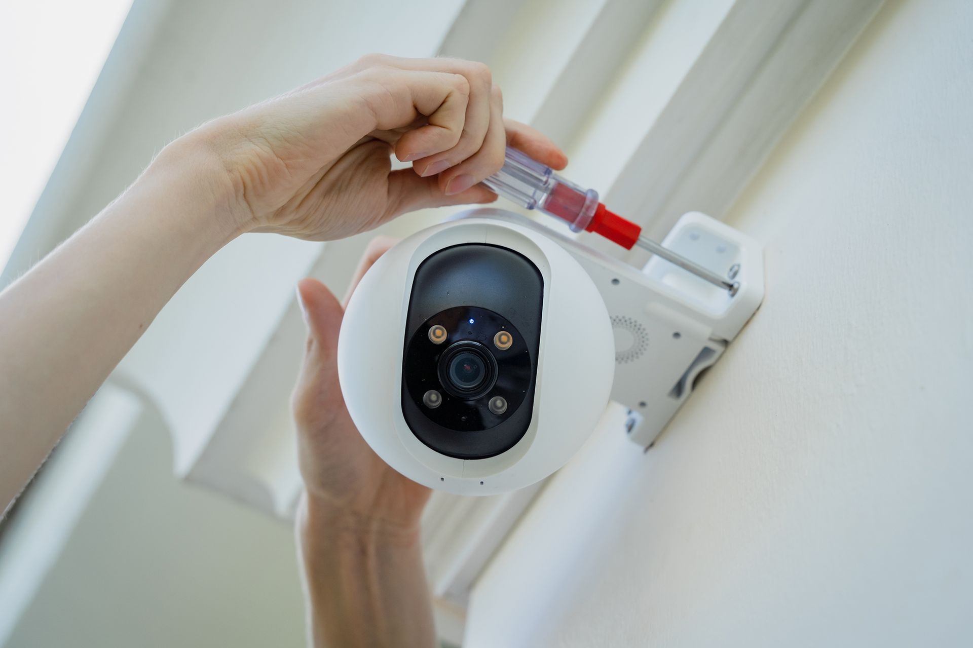 Hand testing a white smoke detector mounted on a white ceiling.