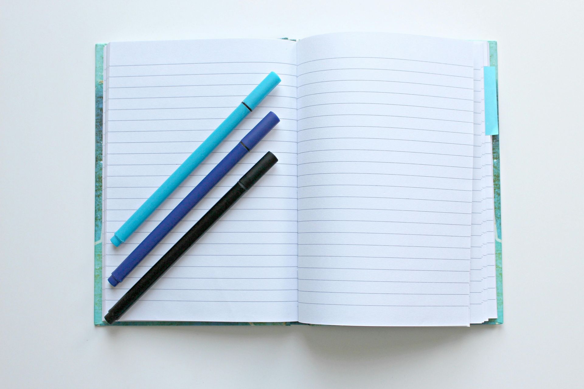 Three pens are sitting on top of an open notebook.