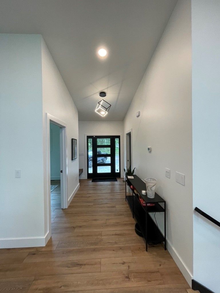 A long hallway with hardwood floors and white walls leading to a door.