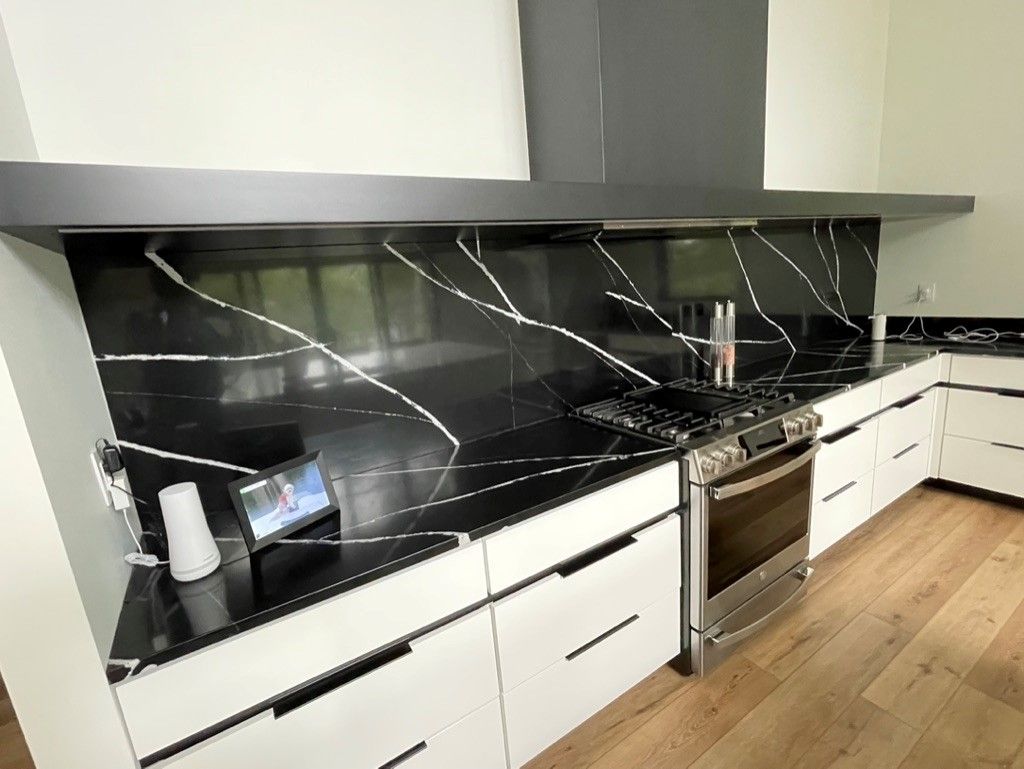 A kitchen with black counter tops , white cabinets , and stainless steel appliances.