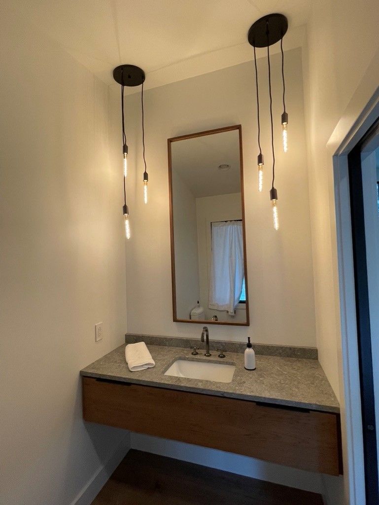 A bathroom with a sink , mirror and lights hanging from the ceiling.