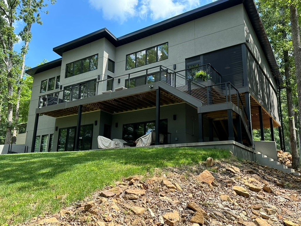 A large house with a large deck is sitting on top of a grass covered hill.