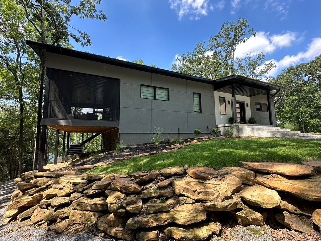 A house with a screened in porch and a stone wall in front of it.