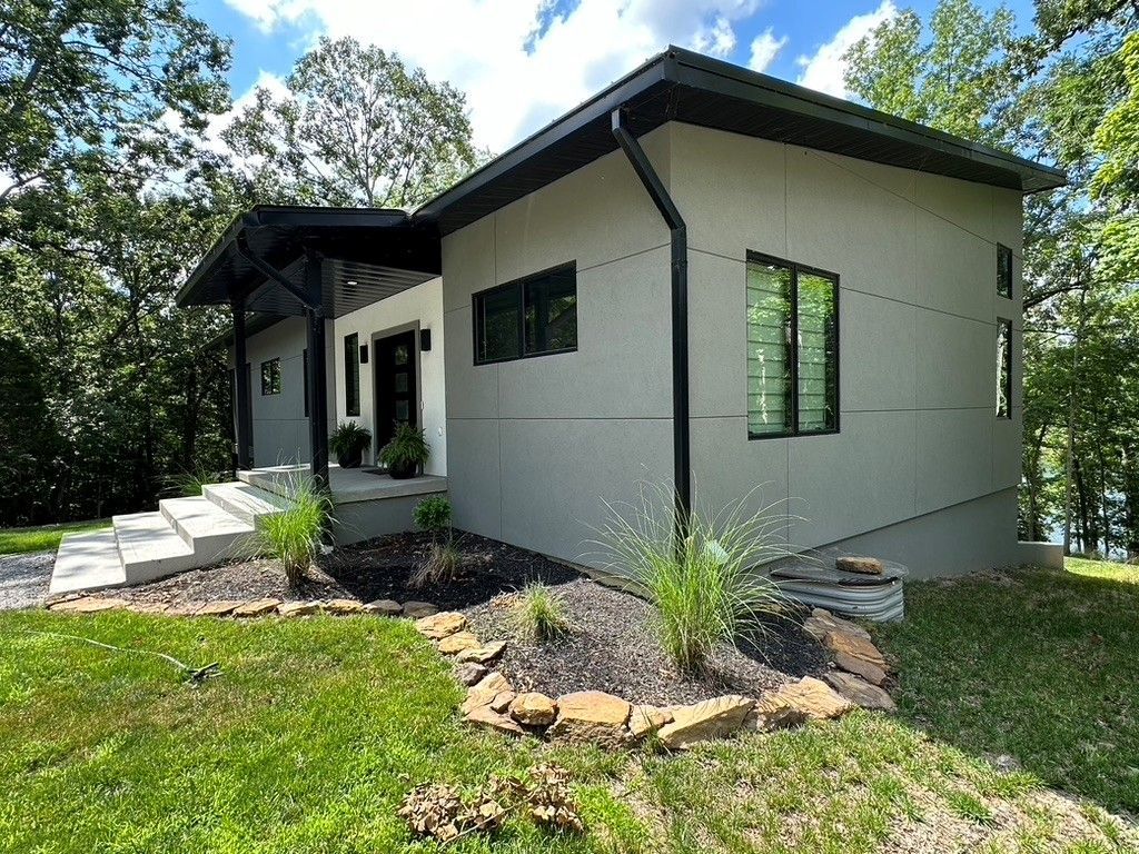 A small white house with a black roof is sitting on top of a lush green hill.