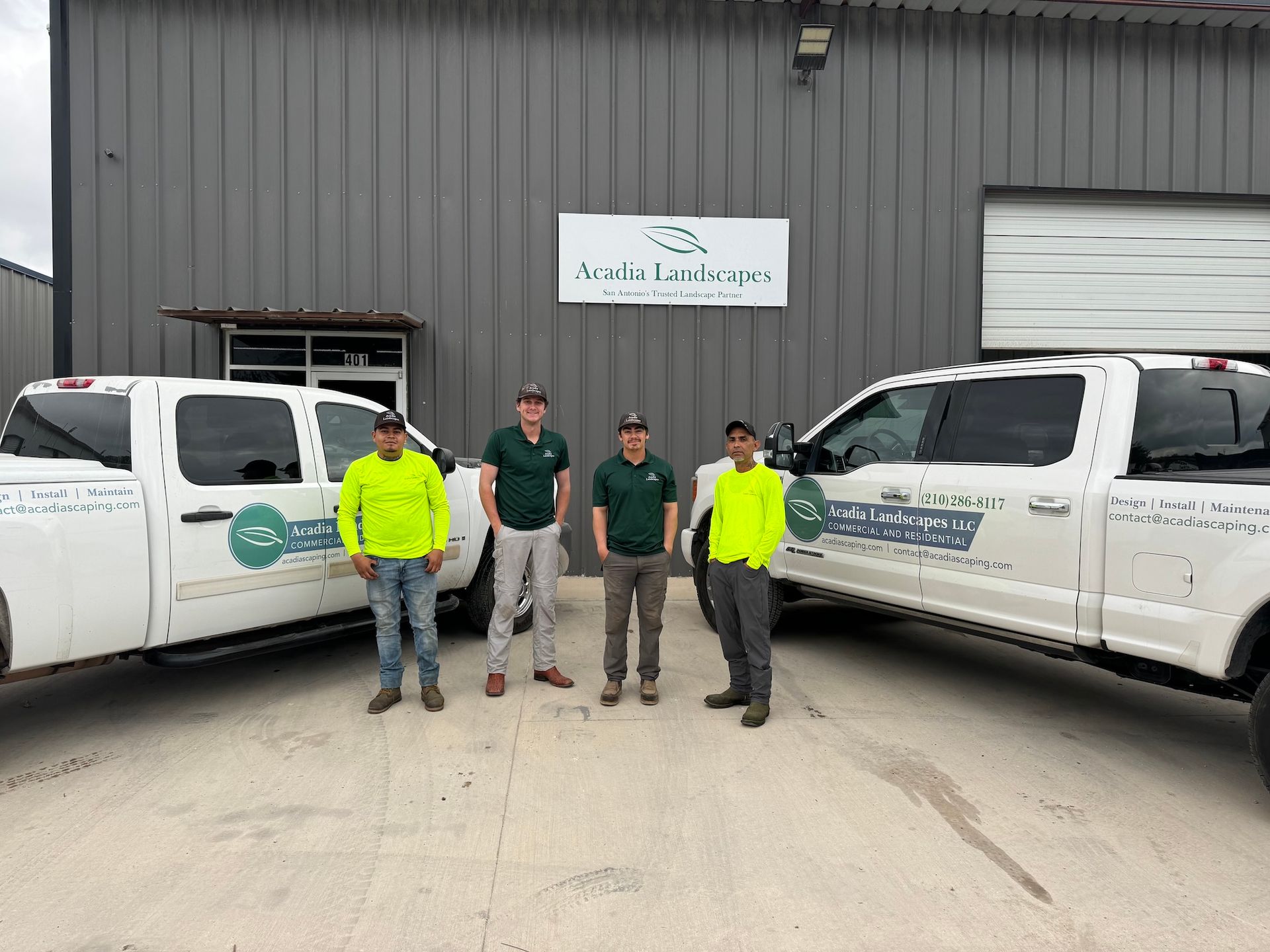 Four people in work attire stand between two white pickup trucks in front of a building with a company sign.