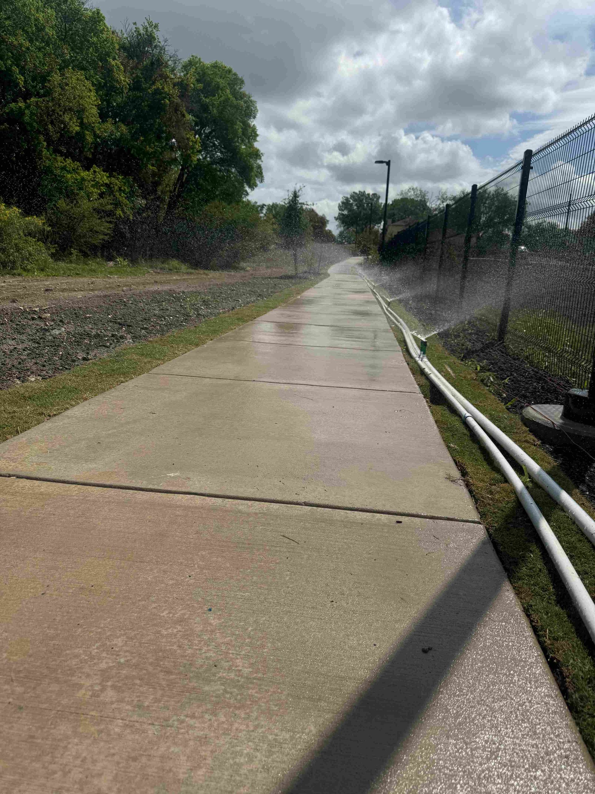 Sprinklers watering a small landscaped area with green grass and mulch.