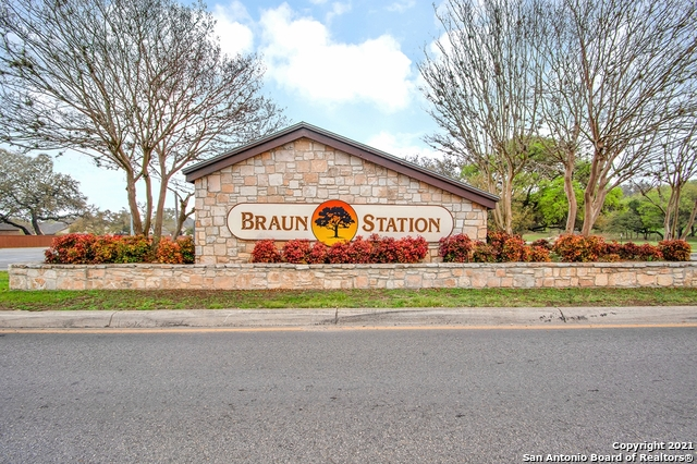 Stone entrance sign for Braun Station, with an orange tree logo, set against a blue sky, surrounded by shrubbery.