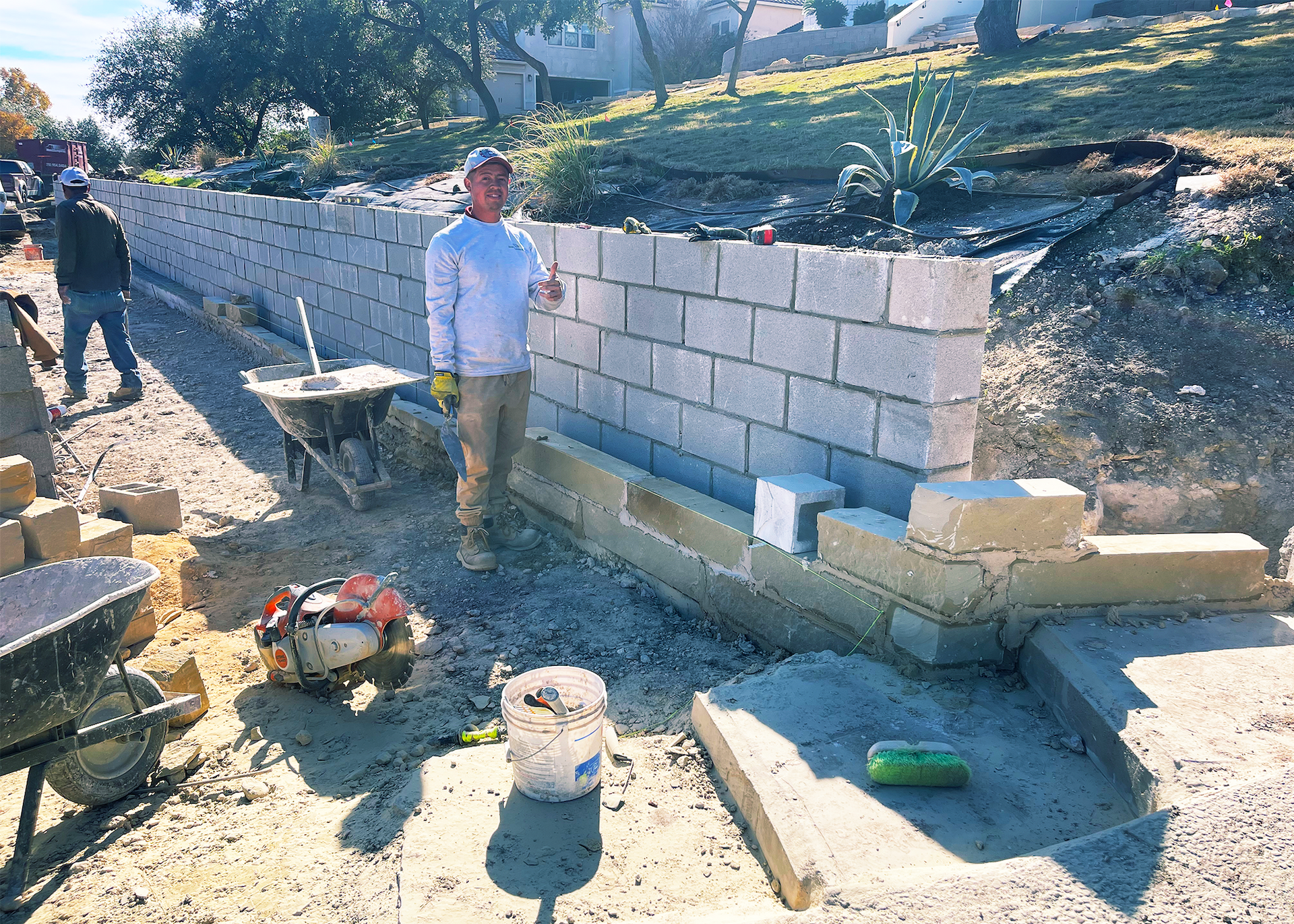Construction worker by a retaining wall made of concrete blocks; outdoors.