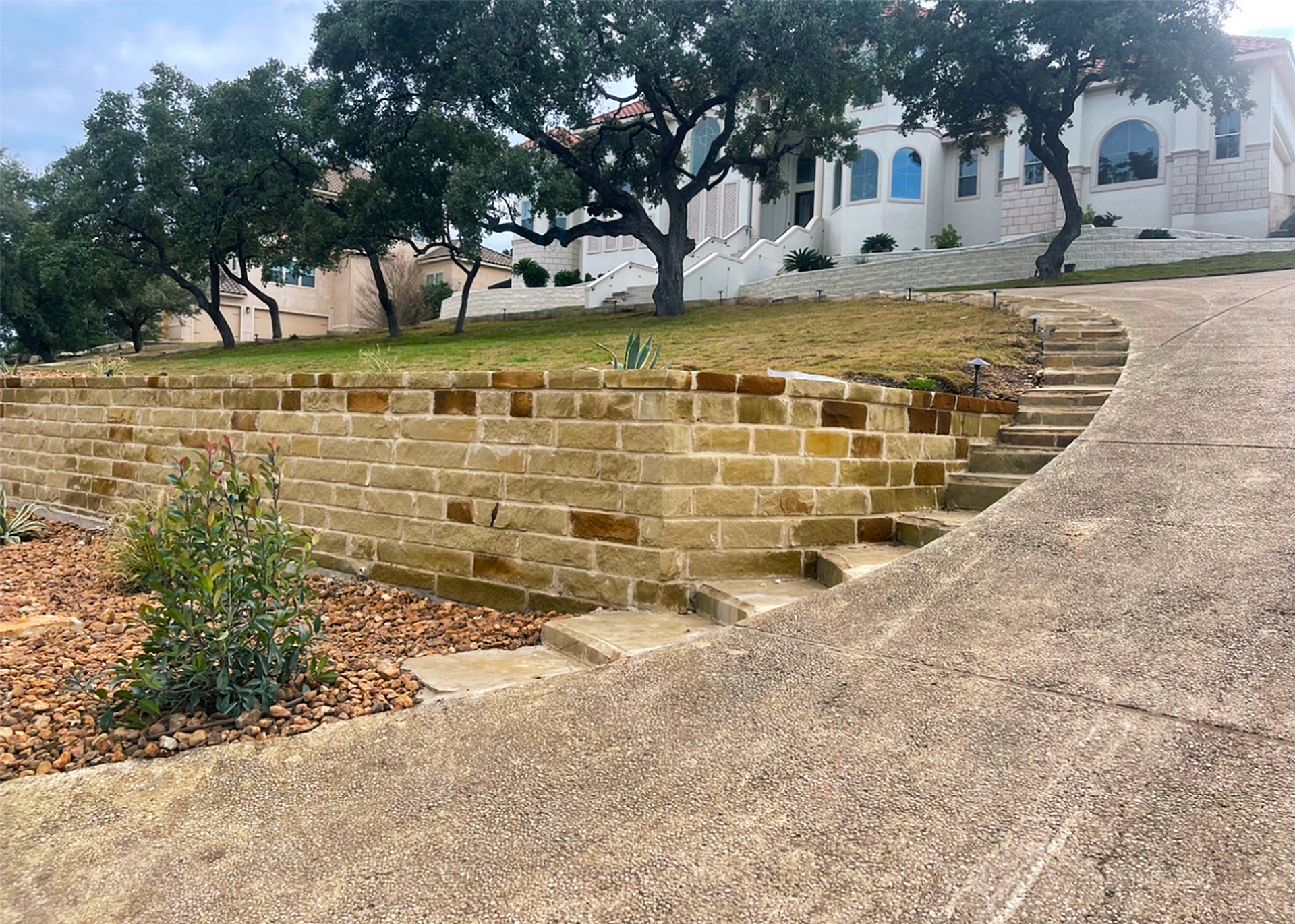 Stone steps and retaining wall leading to a multi-story house on a hillside.