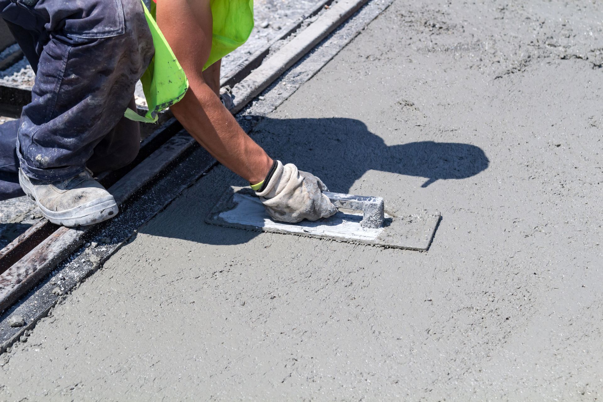 Worker smoothing wet pavement with a trowel on a road surface