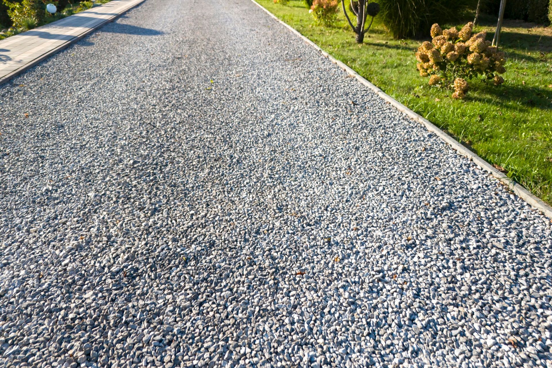 Gravel path bordered by green grass and shrubs in a sunny outdoor park area