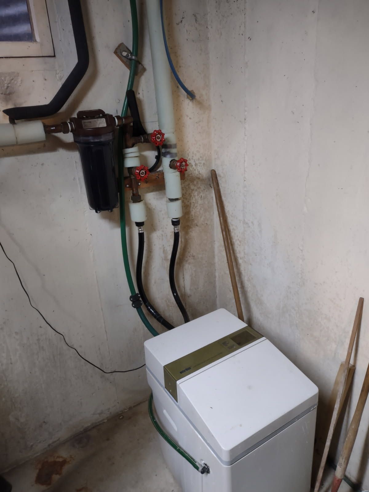 Laundry area with washing machine, water pipes, and wall-mounted plumbing filters in a small utility room
