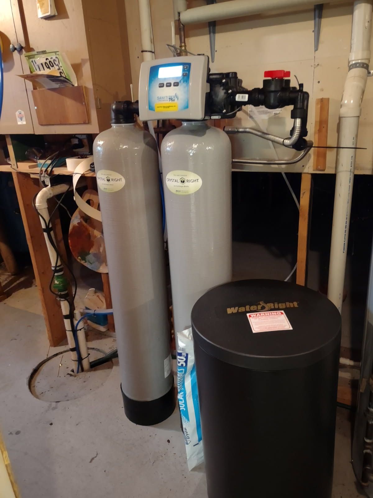 Two gray water softener tanks and a black filter tank in a utility room