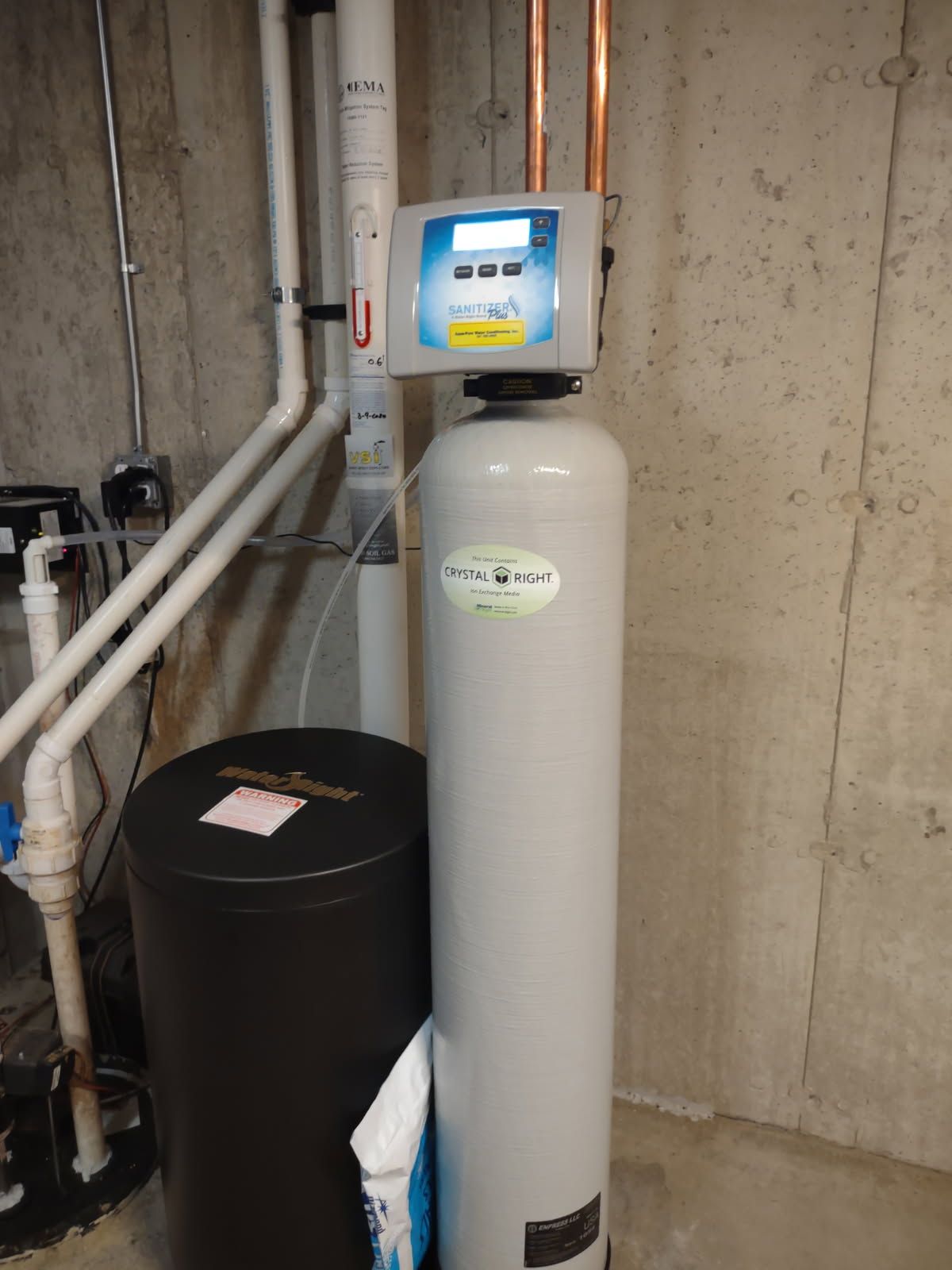 Tall gray water softener tank with digital control panel in a basement utility room.