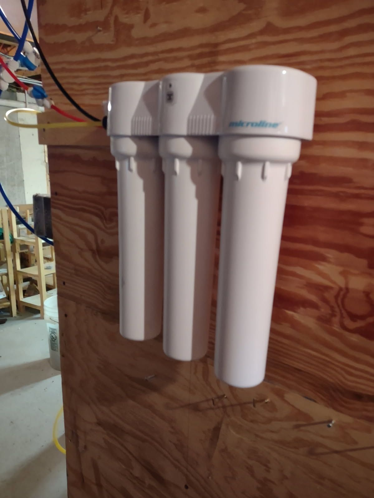 Three-cartridge white water filter mounted on a plywood wall with exposed plumbing.