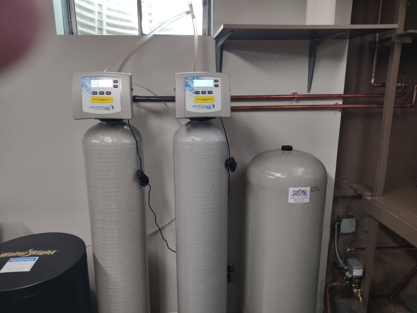 Two gray water softener tanks and a brine tank in a utility room
