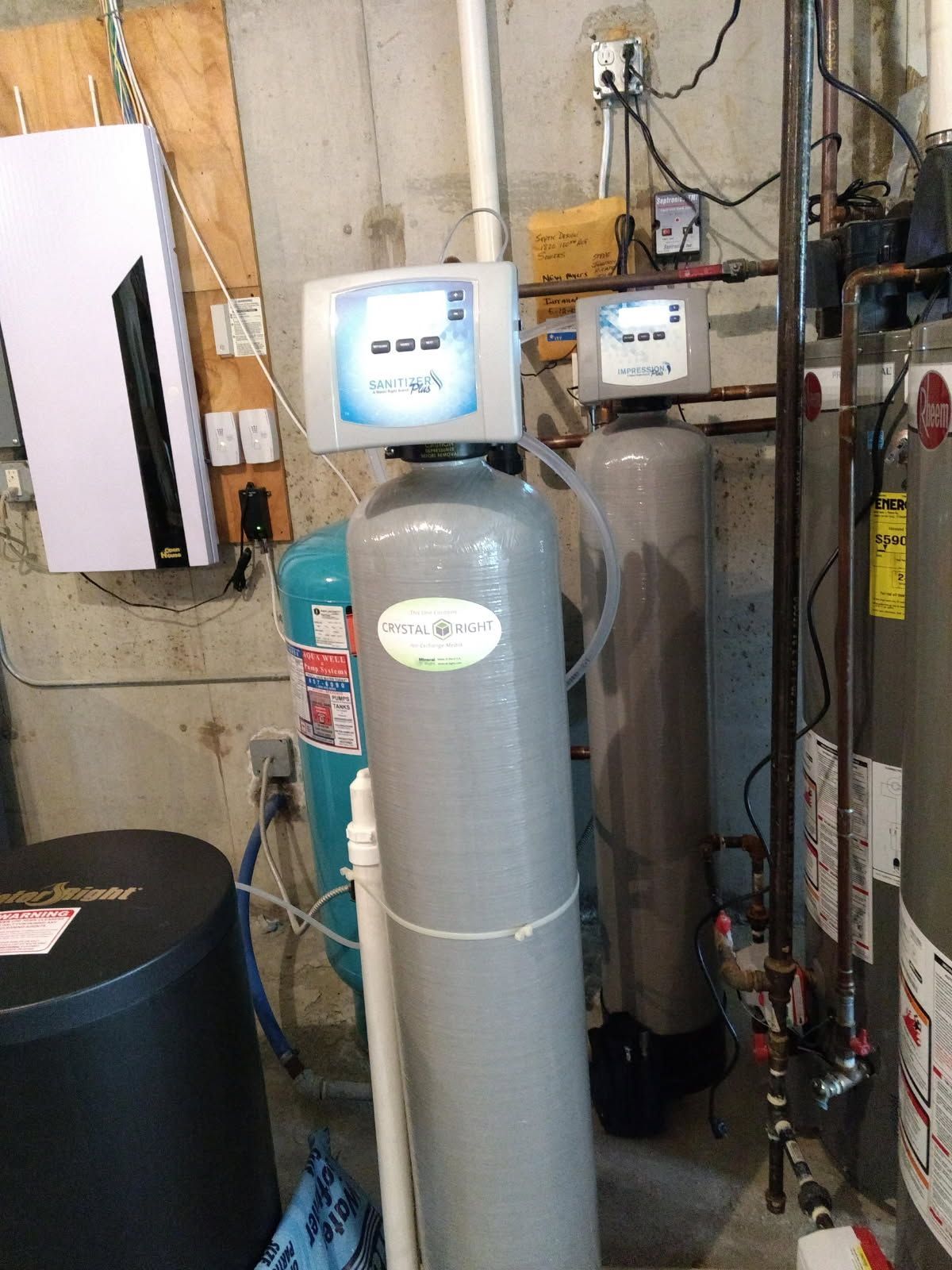 Water softener system and nearby equipment in a utility room with pipes and electrical wiring.