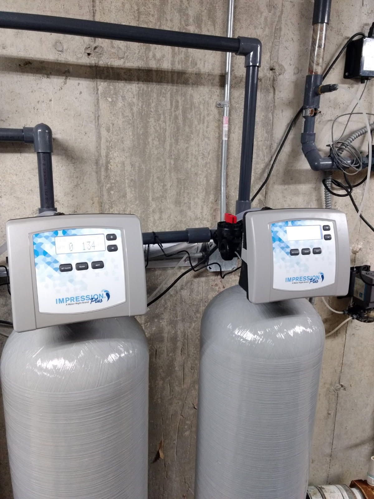 Two white water softener tanks with control heads in a basement utility area.