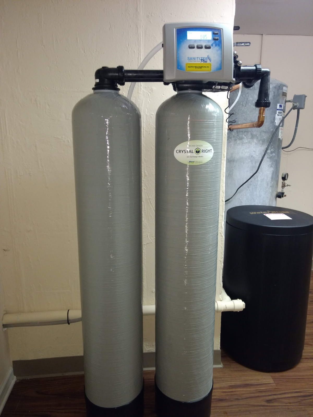 Water softener and filtration tanks in a basement utility area, with gray cylinders and a black tank.