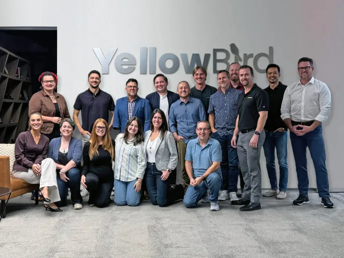 YellowBird team posing in front of the company sign in a lobby.