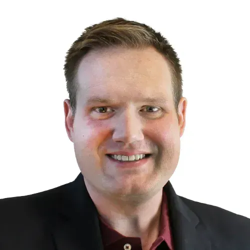 Smiling man in a dark blazer and maroon shirt against a white background